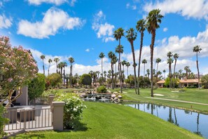 Un campo de golf con un estanque, palmeras y un club de campo con terraza.
