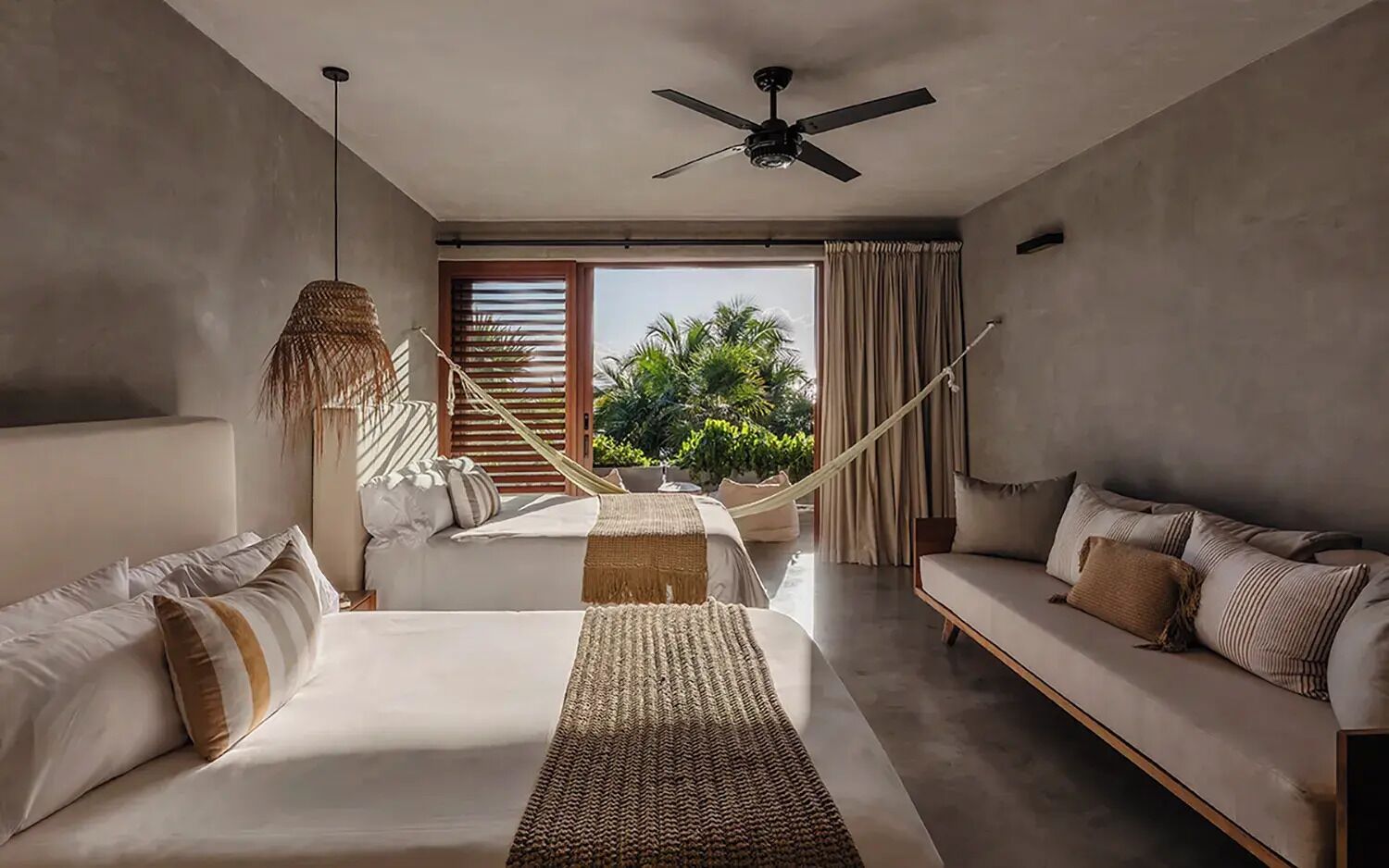 A modern bedroom with a large bed, a sofa, a hammock, and a view of greenery outside.