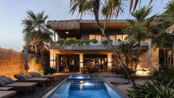 A modern house with a pool, outdoor seating, and tropical plants.