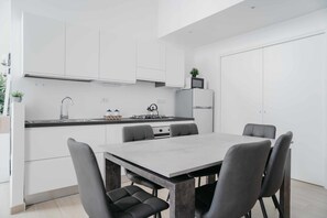 A modern kitchen with white cabinets, a dining table with chairs, and a built-in stove.
