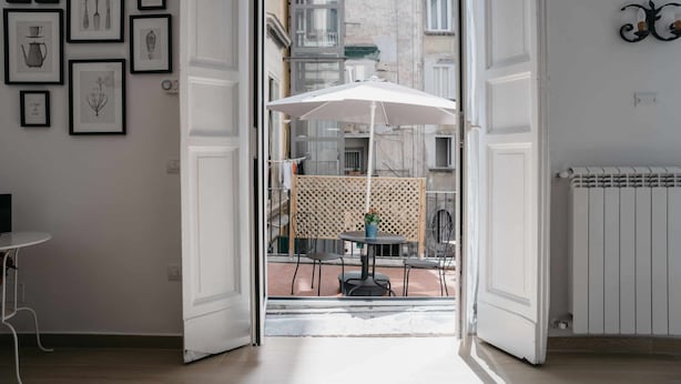 An open doorway leading to an outdoor patio with a table and chairs, a white umbrella, and framed pictures on the wall. - Nilo – Historic Apartment with Patio by Casa N (Napoli)