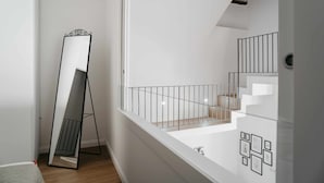 A modern room with a large mirror, a staircase, and a white wall with framed pictures. - Nilo – Historic Apartment with Patio by Casa N (Napoli)