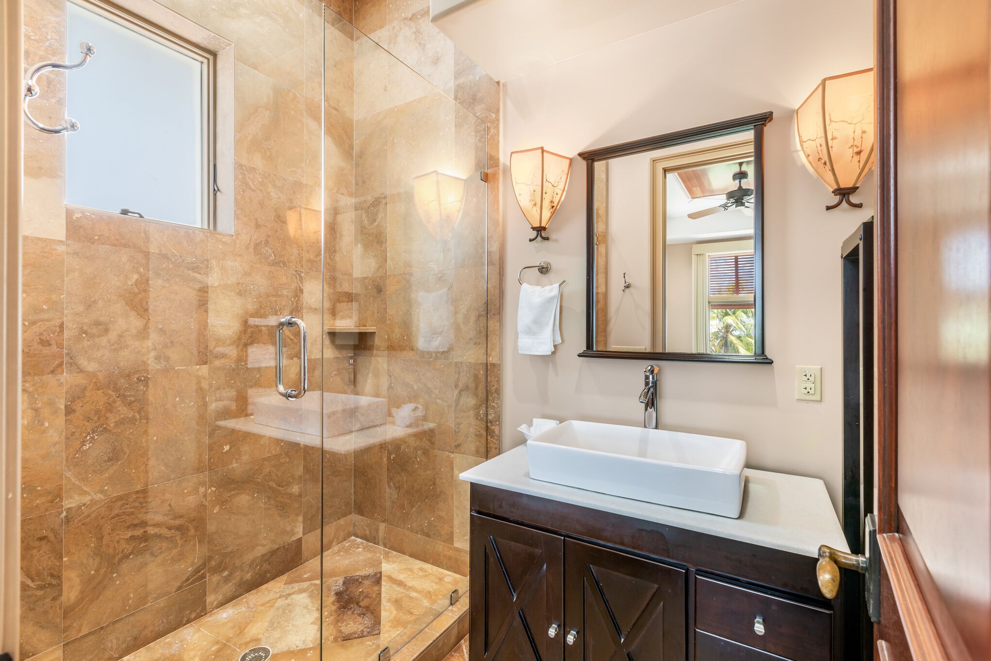 A modern bathroom with a glass-enclosed shower, a white sink, dark wooden cabinets, and wall-mounted lighting.