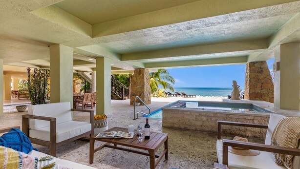 A spacious indoor area with a view of the ocean, featuring a pool, seating areas, and a stone pillar. - ✦Unwind on your Oceanedge villa on Seapalm island✦ (Little Conch Key)