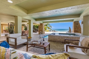 A spacious indoor area with a view of the ocean, featuring a pool, seating areas, and a stone pillar.