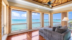 A spacious room with large windows offering ocean views, a ceiling fan, and a grey sofa. - ✦Unwind on your Oceanedge villa on Seapalm island✦ (Little Conch Key)