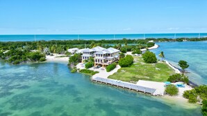 A large, multi-story house with a spacious deck and a private dock, surrounded by clear blue waters and lush greenery. - ✦Unwind on your Oceanedge villa on Seapalm island✦ (Little Conch Key)