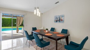 A dining area with a large table, teal chairs, and a view of a pool through glass doors.