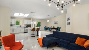 A modern living room with a blue sofa, an orange armchair, and a dining area with blue chairs.
