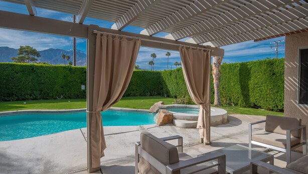 A covered outdoor area with a pool, seating, and a view of mountains.