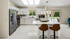 A modern kitchen with white cabinets, a central island, and a view of a garden through the window.