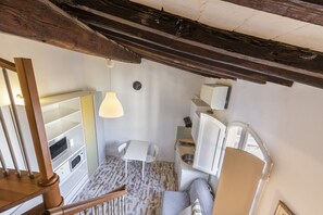 Een compacte kamer met houten plafond, een tafeltje, een stoel, een bed en een witte kast.