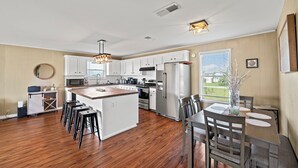 Una cocina amplia con una isla central, armarios blancos, electrodomésticos de acero inoxidable y un comedor con mesa y sillas.