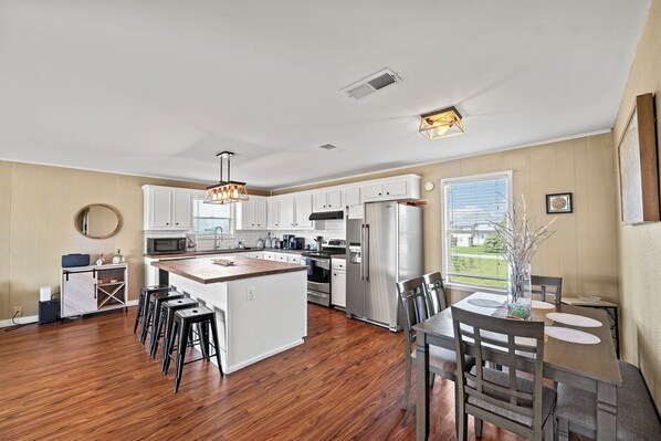 A spacious kitchen with a central island, white cabinetry, stainless steel appliances, and a dining area with a table and chairs.