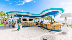 An outdoor seating area with a curved blue and white roof, orange chairs, and a white lamp post. - Modern Beach Highrise  Ocean Walk Resort 1 BR Ocean View W/Jacuzzi Daytona Beach (Daytona Beach)