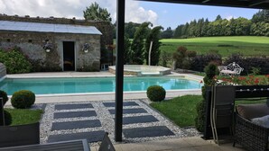 Zona de piscina con un edificio de piedra, un jacuzzi y vistas a un campo verde.