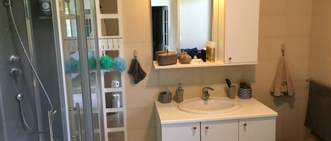 A bathroom with a glass shower enclosure, a sink, a mirror, and a vanity with storage cabinets.