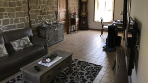 Una sala de estar con pared de piedra, un mueble de madera, un sofá, una mesa de centro y un reloj.