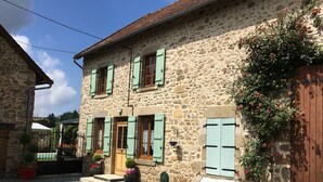 Un edificio de piedra con contraventanas verdes, una puerta de madera y un camino de entrada de grava.