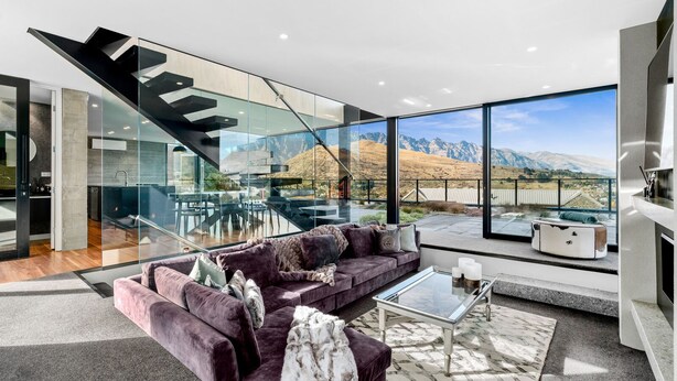 A modern living room with a large glass wall, a purple sofa, a glass coffee table, and a view of mountains. - 1 St. Marks (Queenstown)