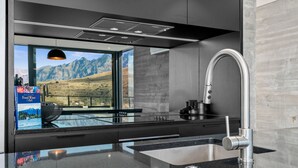 A modern kitchen with a large window offering a mountain view, a sleek faucet, and a book titled "New Zealand Food Wine Art" on the counter. - 1 St. Marks (Queenstown)