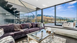 A modern living room with a glass coffee table, a purple sofa, and a view of mountains through large windows. - 1 St. Marks (Queenstown)