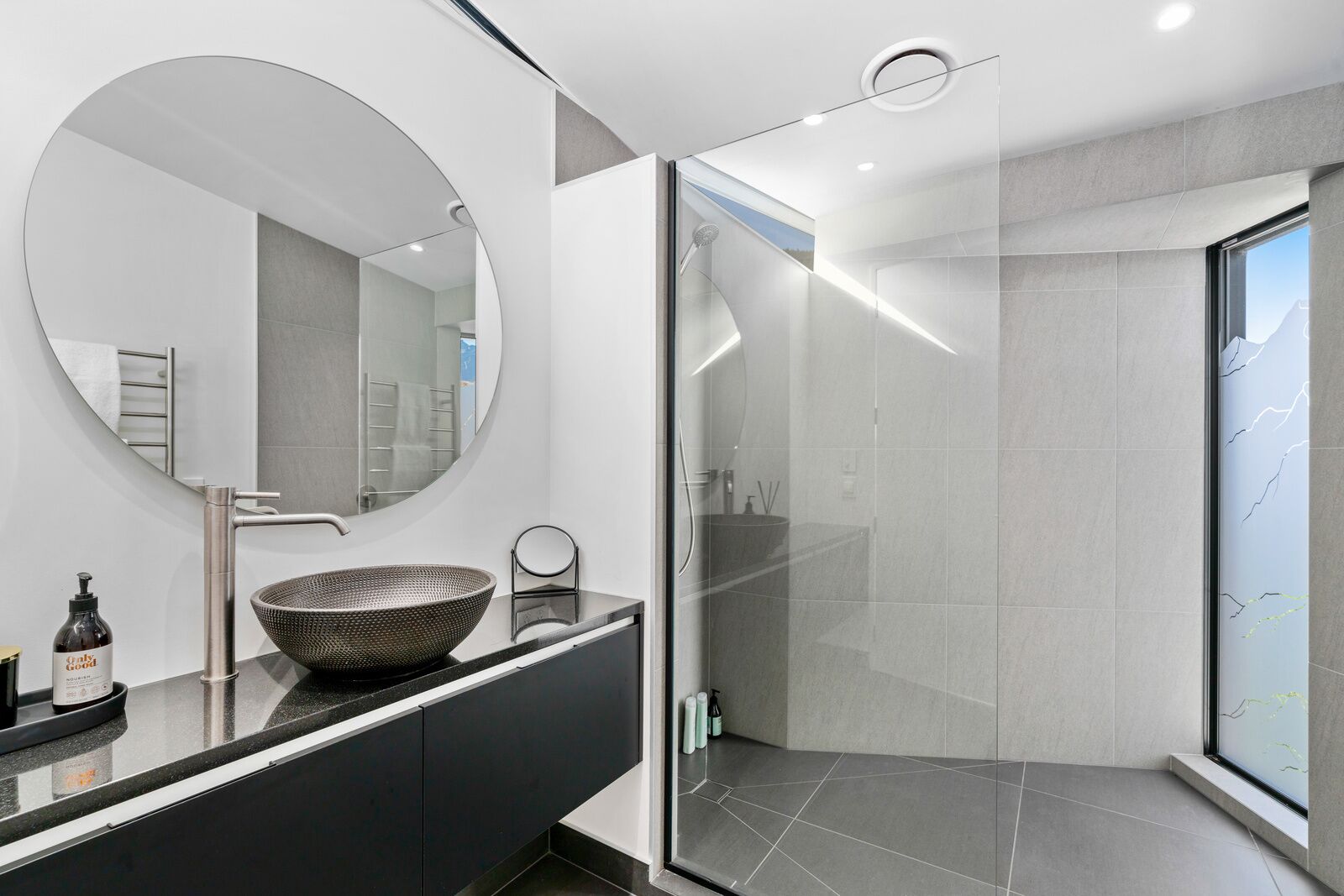 A modern bathroom with a round mirror, a large vessel sink, and a walk-in shower.