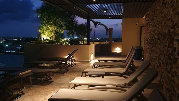 An outdoor seating area with lounge chairs and tables, a covered roof, and a view of the city at dusk. - Syren 401 (Playa del Carmen)