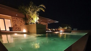 A nighttime view of a swimming pool with a stone wall and a palm tree. - Syren 401 (Playa del Carmen)