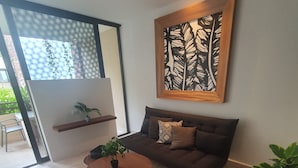 A modern living room with a dark brown sofa, a round wooden coffee table, and a black armchair. There is a large abstract art piece on the wall, a potted plant on the coffee table, and another on the armchair. - Syren 401 (Playa del Carmen)