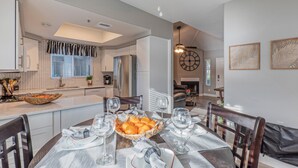 Zona pranzo con tavolo apparecchiato per sei persone, cucina sullo sfondo e soggiorno visibile attraverso una porta aperta.