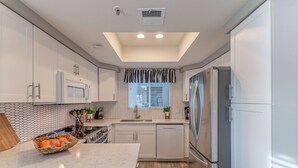 Una cucina moderna con mobili bianchi, un'isola centrale con un cesto di frutta, elettrodomestici in acciaio inossidabile e un lucernario.
