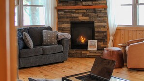 A cozy living room with a stone fireplace, a flat-screen TV mounted above it, and a comfortable sofa with cushions. - Premier Location on Crosslake - Hot Tub - Pontoon Rental - Waterslide - Games  (Crosslake)