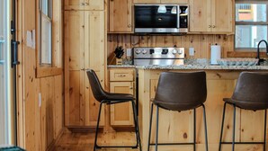 A wooden cabin interior with a kitchen area, bar stools, and a leather couch. - Premier Location on Crosslake - Hot Tub - Pontoon Rental - Waterslide - Games  (Crosslake)