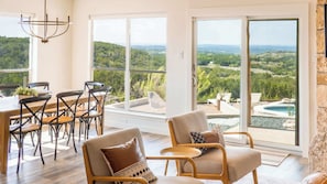 A spacious room with a dining area, large windows, and a view of a pool and landscape. - Pool, Hot Tub, Putting Green | 8 Acre Retreat (Dripping Springs)
