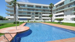 A modern hotel with a swimming pool, multiple balconies, and palm trees. - Apartment for rent in Roses, Costa Brava! Ideal for 4 people, with pool and WiFi. Book now! (Roses)