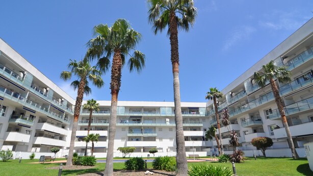 A modern multi-story hotel with a central courtyard featuring palm trees and a well-maintained lawn. - Apartment for rent in Roses, Costa Brava! Ideal for 4 people, with pool and WiFi. Book now! (Roses)