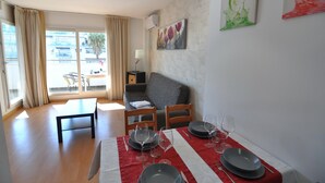 A dining area with a table set for four, a sofa, and a window with curtains. - Apartment for rent in Roses, Costa Brava! Ideal for 4 people, with pool and WiFi. Book now! (Roses)