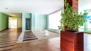 Un hall spacieux doté d’un plancher en bois, d’une grande plante en pot et d’un espace recouvert de petits galets, agrémenté de deux éléments décoratifs sphériques.