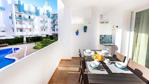 Un balcon avec une table à manger pour quatre personnes, donnant sur une piscine et un quartier résidentiel.