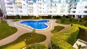 Un immeuble d’appartements moderne doté d’une piscine centrale, entouré de jardins et de sentiers bien entretenus.
