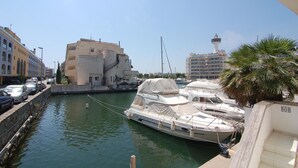 A marina with boats docked, a building with a balcony, and a palm tree. - Charming apartment for rent in Empuriabrava, Costa Brava. 1100m from the beach, capacity for 4 people. (Empuriabrava)