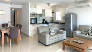 A modern kitchen with white cabinets, a stainless steel refrigerator, and a dining area with a table and chairs. - Charming apartment for rent in Empuriabrava, Costa Brava. 1100m from the beach, capacity for 4 people. (Empuriabrava)