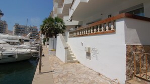 A marina with boats docked, a white building with a stone staircase, and a palm tree. - Charming apartment for rent in Empuriabrava, Costa Brava. 1100m from the beach, capacity for 4 people. (Empuriabrava)