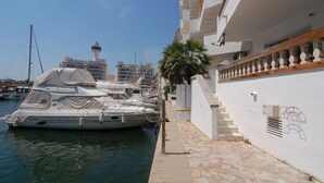 A marina with yachts docked, a white building with a balcony, and a palm tree. - Charming apartment for rent in Empuriabrava, Costa Brava. 1100m from the beach, capacity for 4 people. (Empuriabrava)