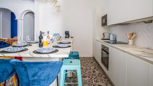 A modern kitchen with white cabinets, a marble countertop, and a patterned floor. There is a dining area with blue chairs and a table set for two. - Appartement Armény - Welkeys (Marseille)