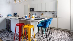 A modern kitchen with white cabinets, a marble countertop, and a central island with stools. - Appartement Armény - Welkeys (Marseille)