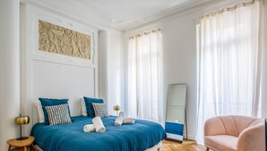 A bedroom with a large bed, a chair, a mirror, and a decorative wall piece. - Appartement Armény - Welkeys (Marseille)