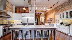 A spacious kitchen with a large island, stainless steel appliances, and a rustic brick wall. - Downtown Luxury Traverse City Loft on Union St (Traverse City)