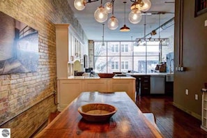 Kitchen features a large island with a wooden bowl, rustic brick accent wall, and stainless steel appliances.